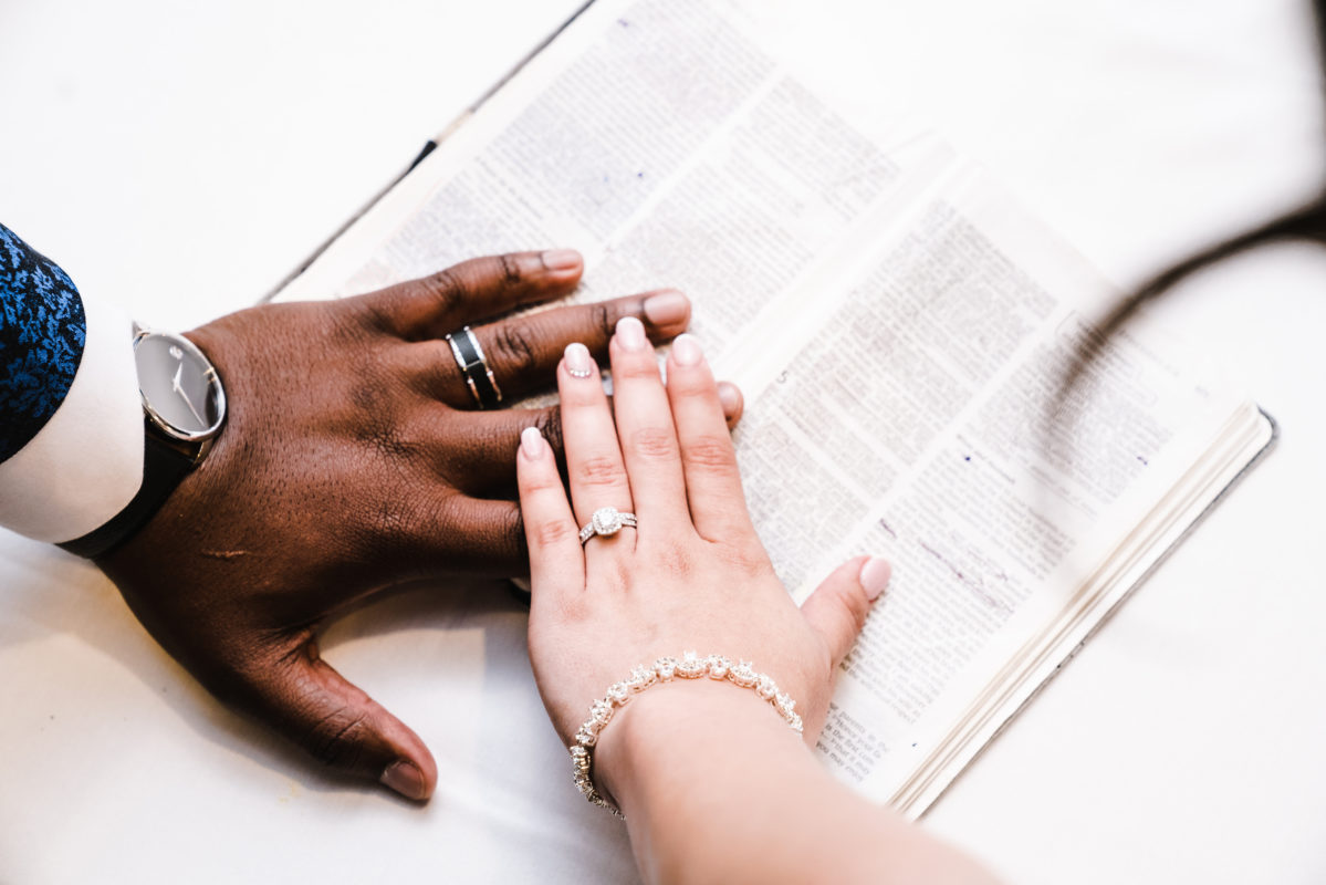 couple placing hand on bible with wedding rings