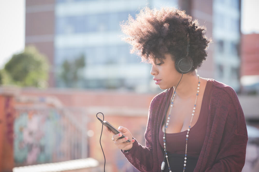 black woman listening to a podcast in headphones while walking in the city
