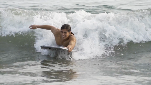 Close up of a Native American man surfing a wave with a boogie board.
