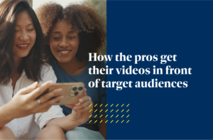 How the pros get their videos in front of their target audiences is shown in white text on top of an image of two women looking at a phone with a dark blue background.