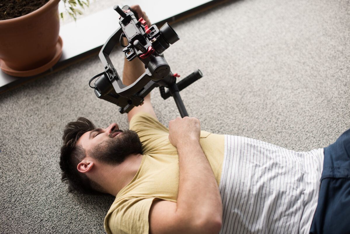 7 basic camera movements. Image of a videographer with a camera on a gimbal filming from the ground.