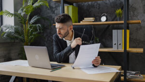 Man looking intensely at laptop screen with paper in his hand at a desk. Motion Array vs Storyblocks